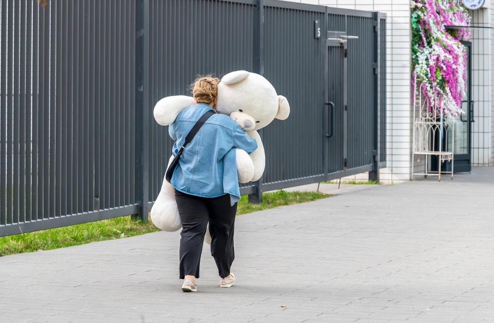 A woman carries a large teddy bear in her arms.