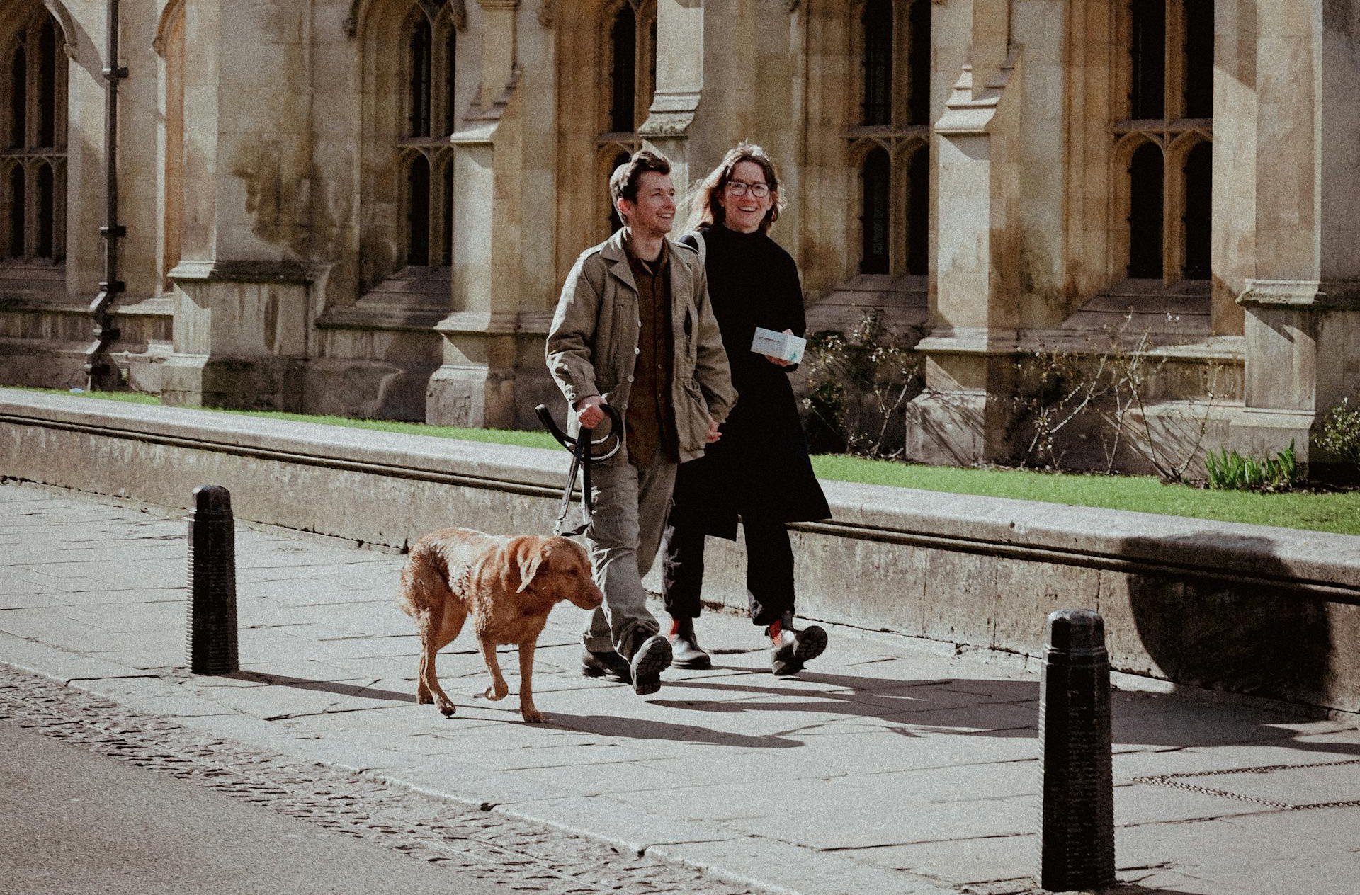 Couple Walking Dog Near Historic Gothic Architecture