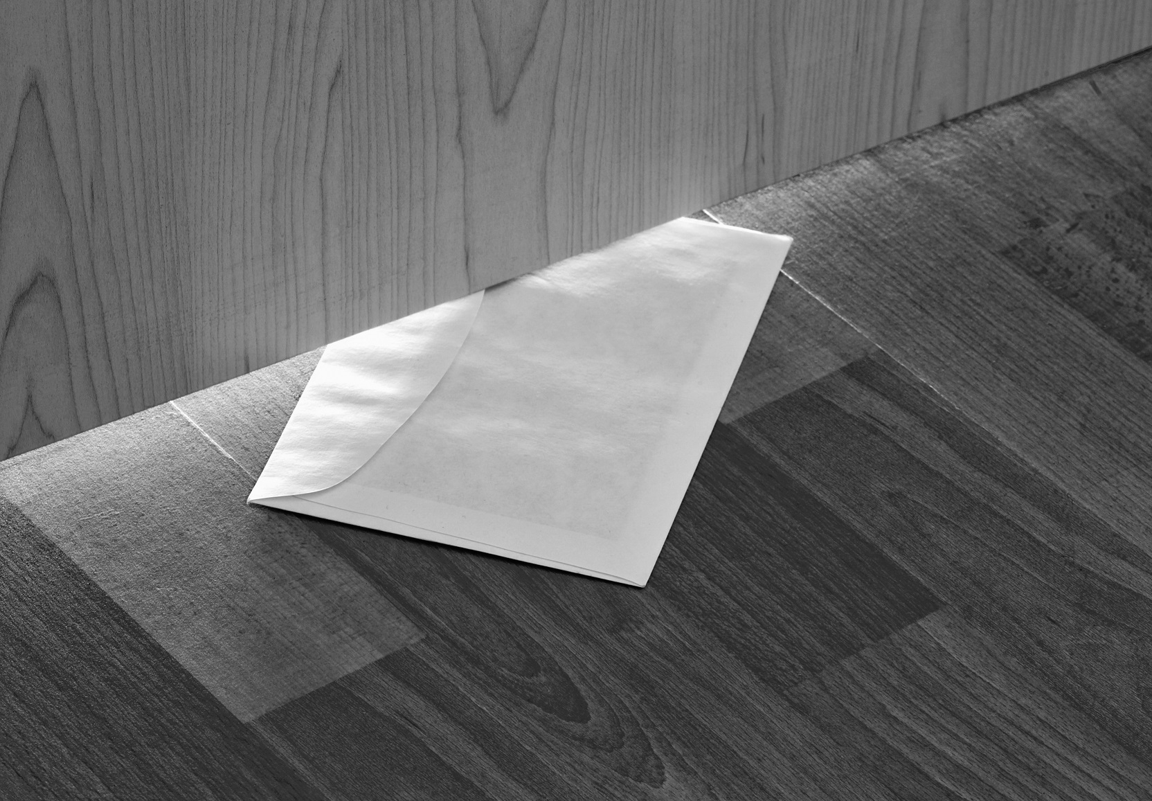 White envelope with message slipped under wooden door.