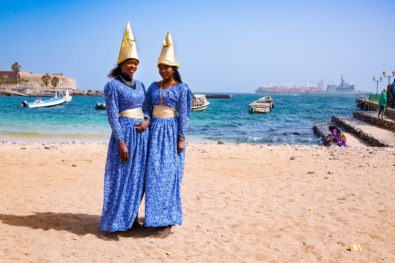 Women in Blue and White Dress and Brown Cone Hats Standing on the Shore - Dakar, Senegal