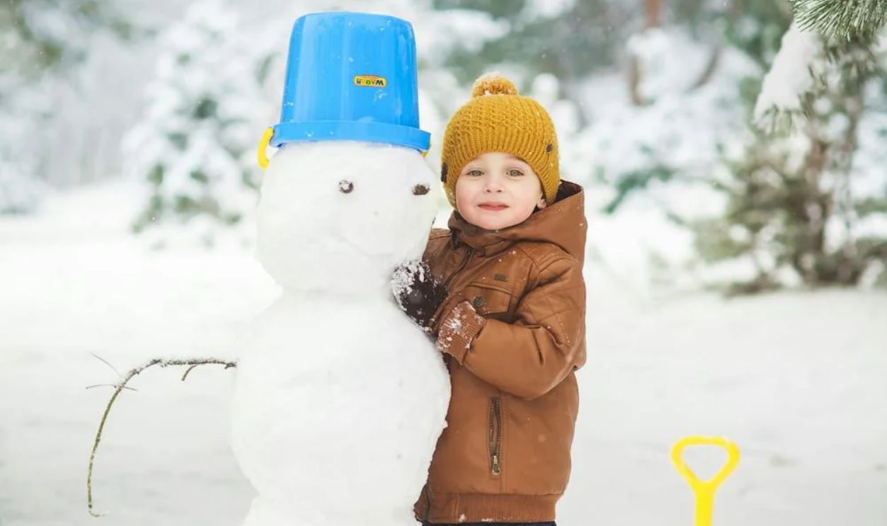 A Boy Playing With a Snowman on Snow Covered Ground