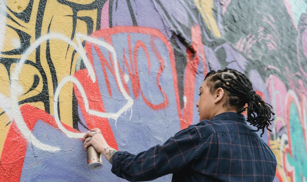 Woman wearing shirt spray painting graffiti on wall