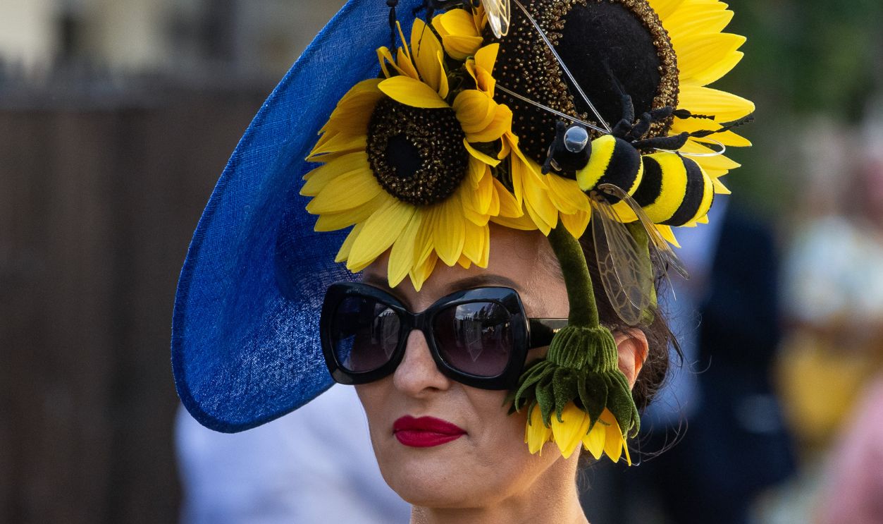 A racegoer wearing a yellow dress and sunflower-and bee-themed hat leaves Royal Ascot on Gold Cup Day on 22 June 2023 in Ascot, United Kingdom. Many spectators for Gold Cup Day, the third day of Royal Ascot which has also been known as Ladies' Day since 1823, wear extravagant hats and outfits.