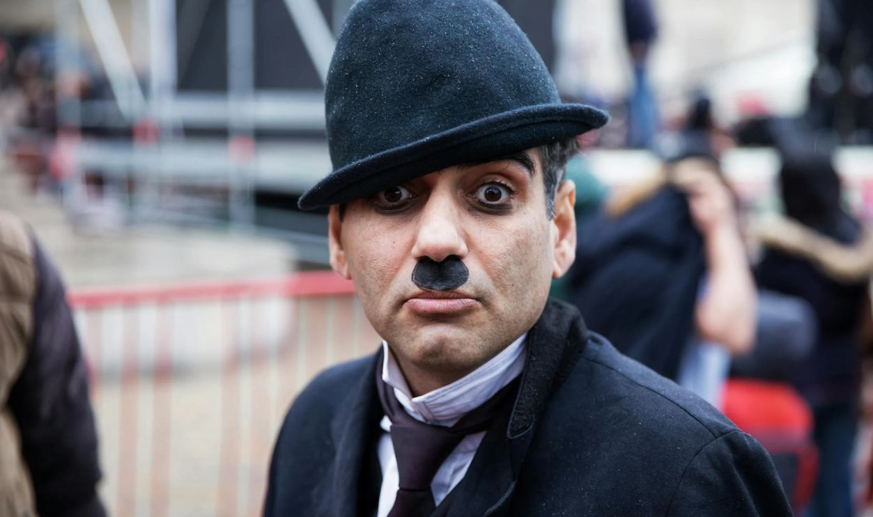 Man with a Mustache, and Wearing a Black Hat, Making a Facial Expression on a Street