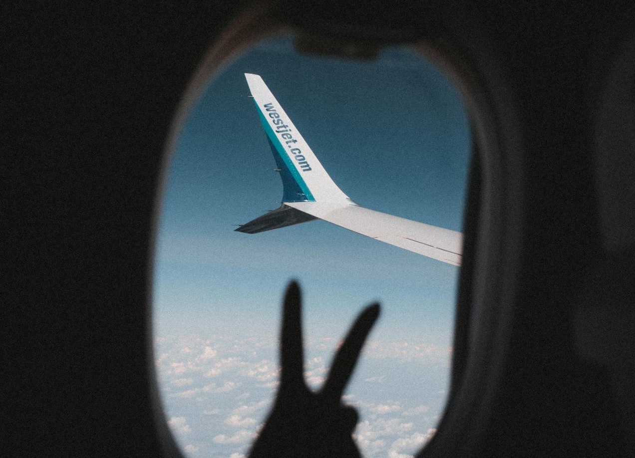 Silhouetted Hand Showing a Peace Sign on the Background of an Airplane Window during a Flight