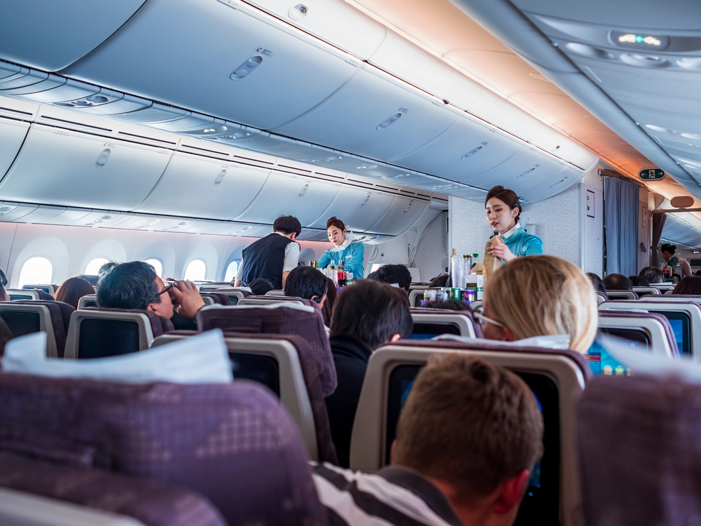 Korean Air cabin crews serving refreshments to seated passengers during flight - 2019