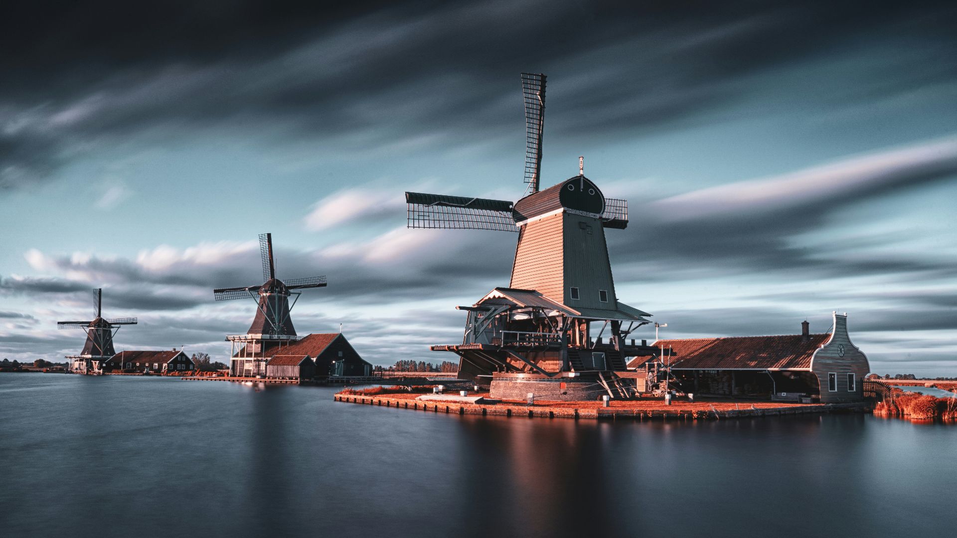 three windmills by the lake under grey cloudy sky