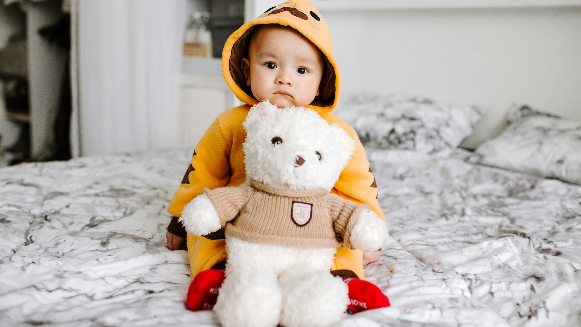 toddler sitting on bed beside white bear plush toy