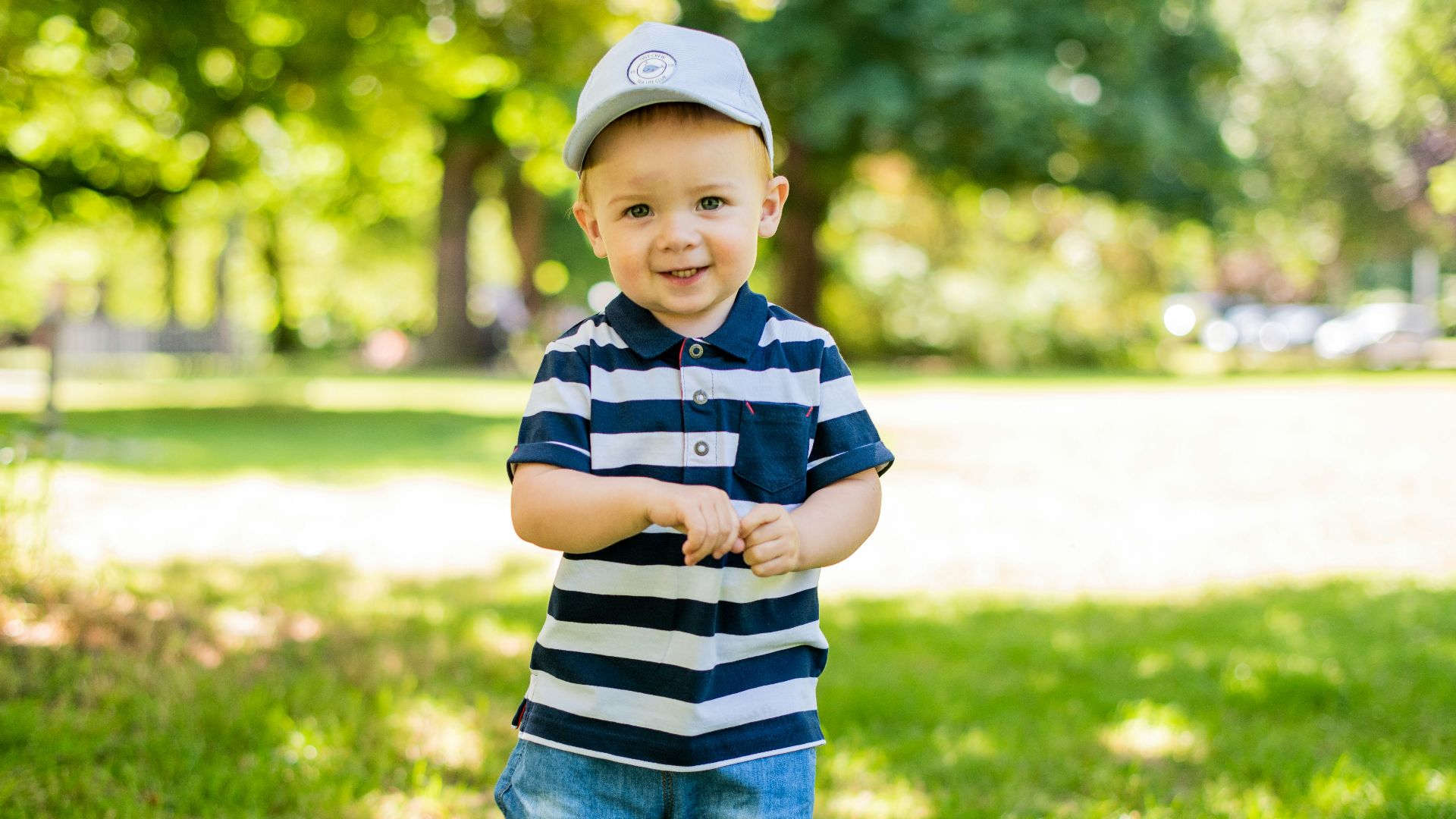 boy in black and white stripe polo shirt and blue denim shorts standing on green grass