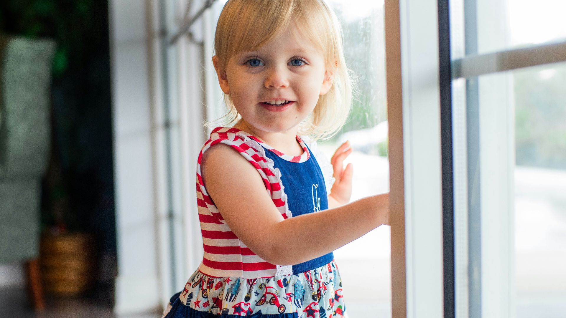 girl in red and white striped tank top and floral skirt standing beside glass window during