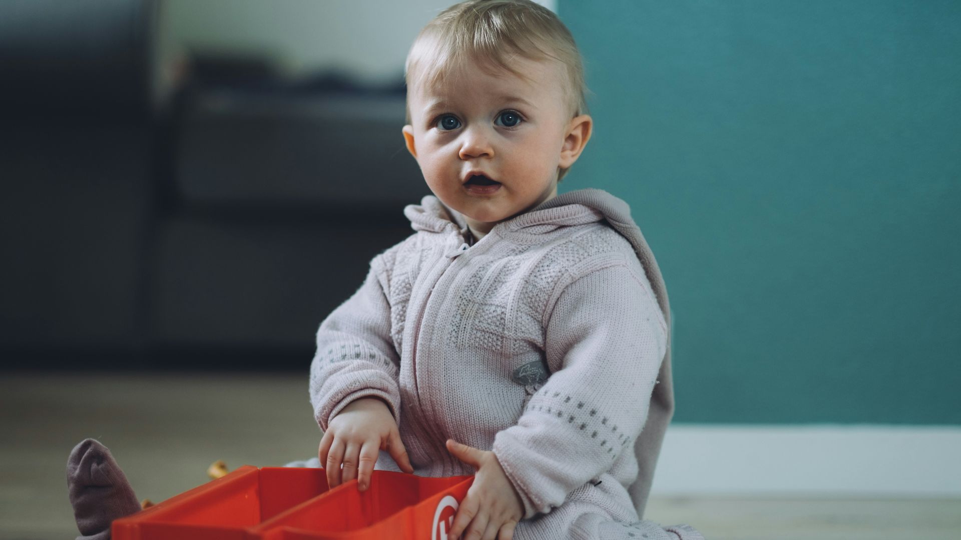 toddler sitting on ground while holding red plastic case