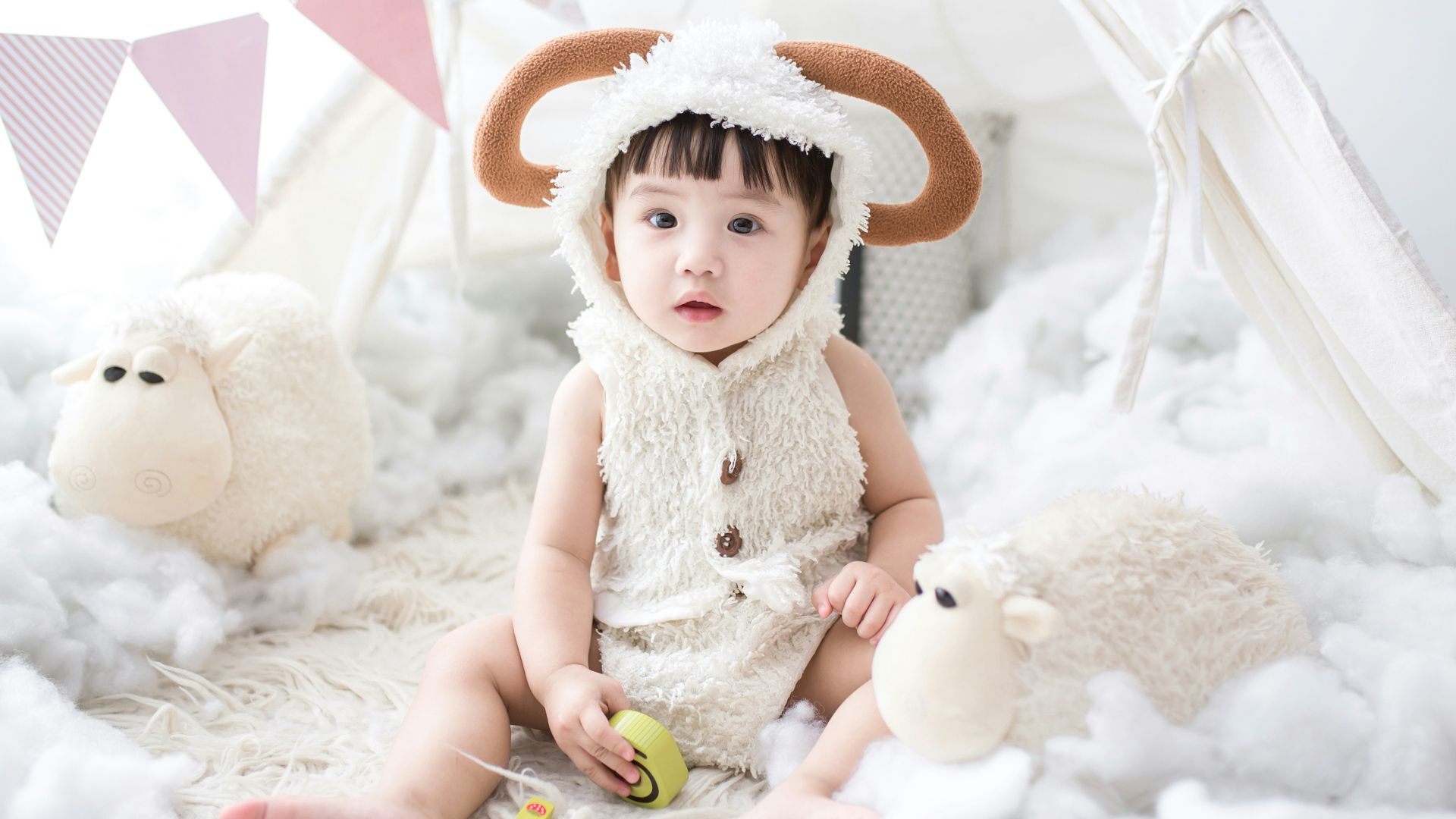 baby sitting beside white sheep plush toy