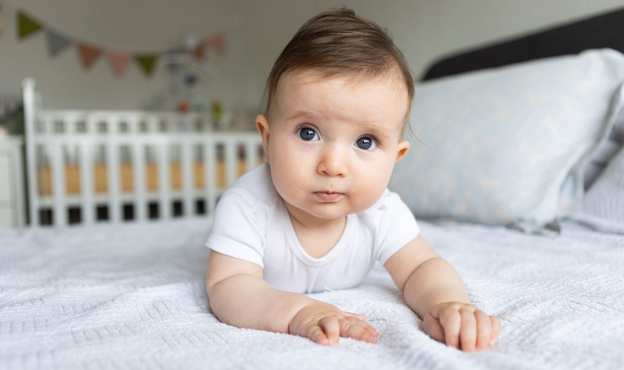 Six months old baby portrait, laying on tummy at bedroom.
