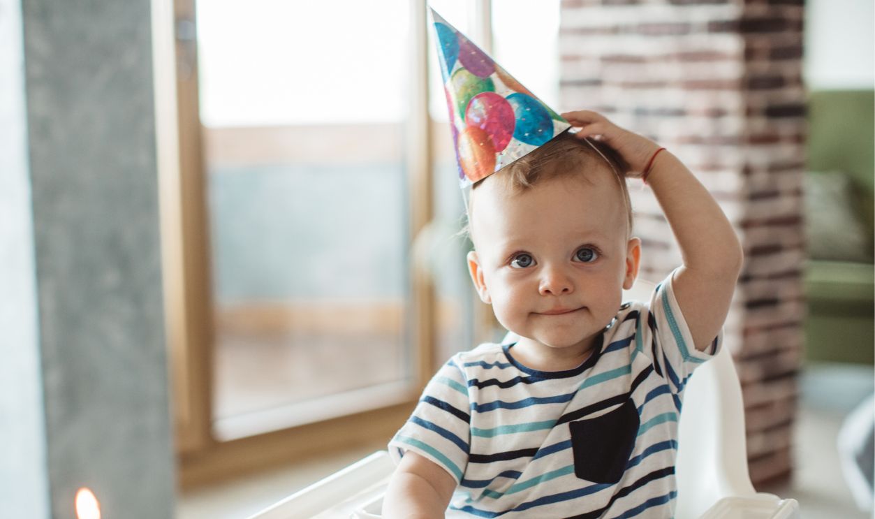 Little boy celebrate first birthday at home, wearing party hats, birthday cake and candle are ready