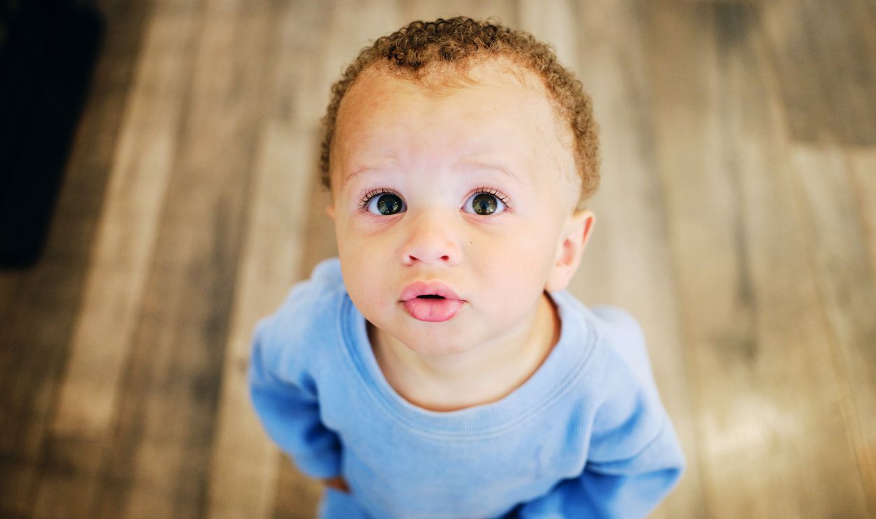 A one year old baby boy looking up at the camera.