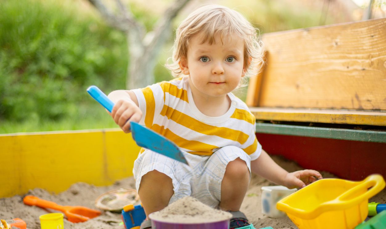 A little boy playing in the sandbox at the playground outdoors. Toddler playing with sand molds and making mudpies. Outdoor creative activities for kids.