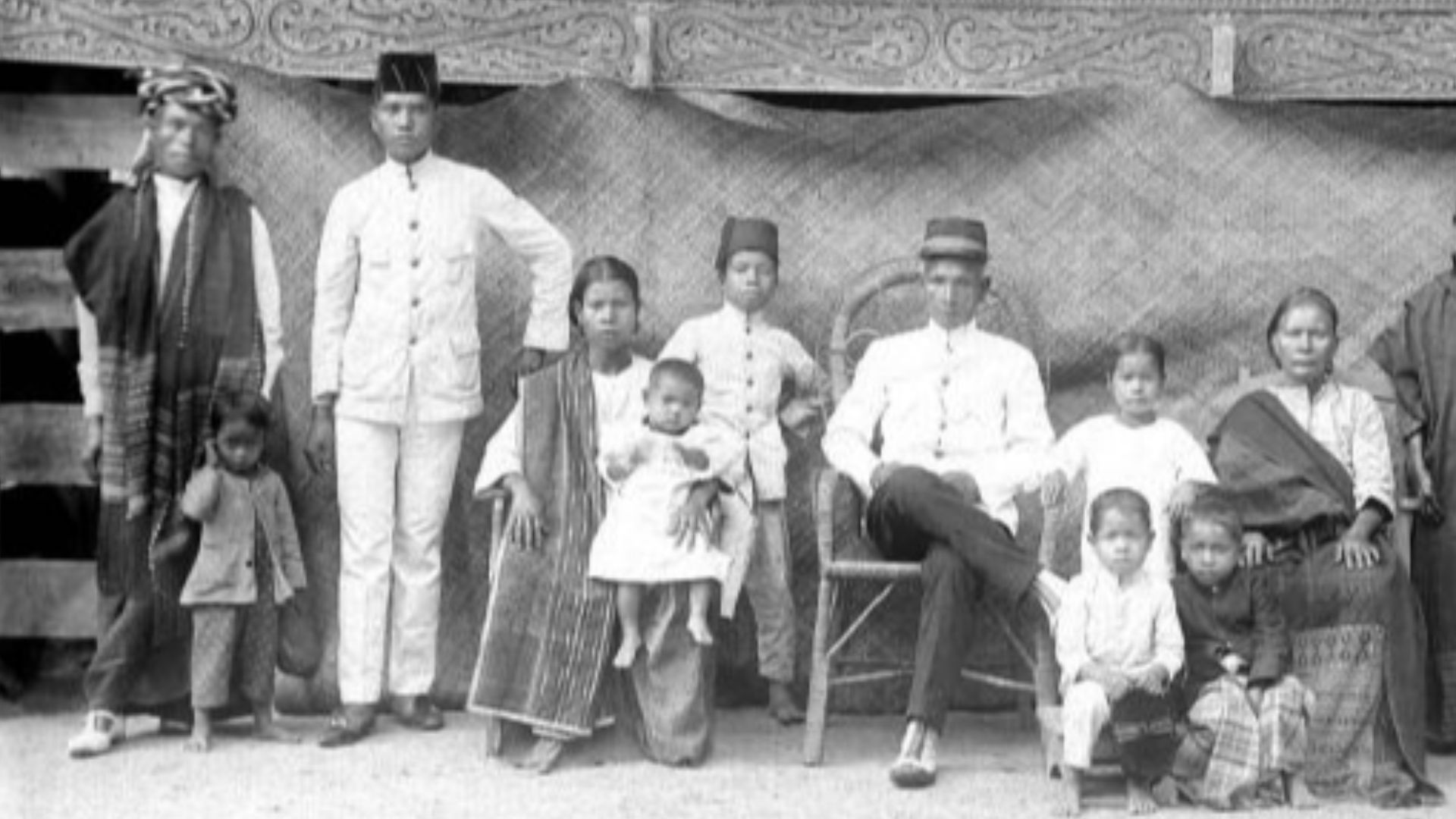 File:COLLECTIE TROPENMUSEUM Toba-Bataks hoofd met zijn familie voor hun met fraai houtsnijwerk versierde huis TMnr 10001701.jpg