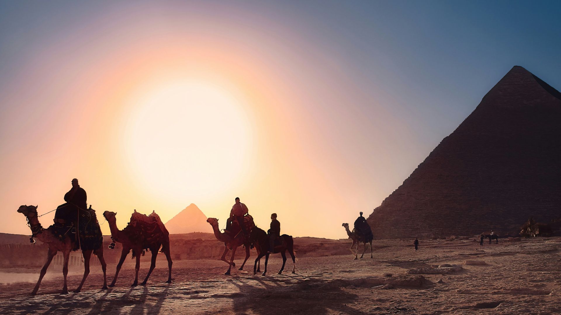 five persons riding camels walking on sand beside Pyramid of Egypt
