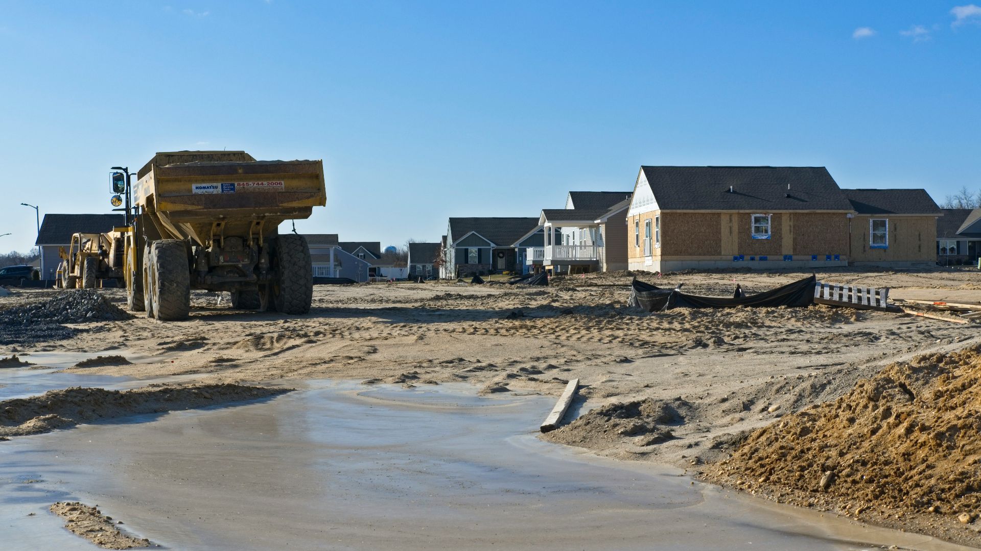 a construction site with a dump truck and houses in the background