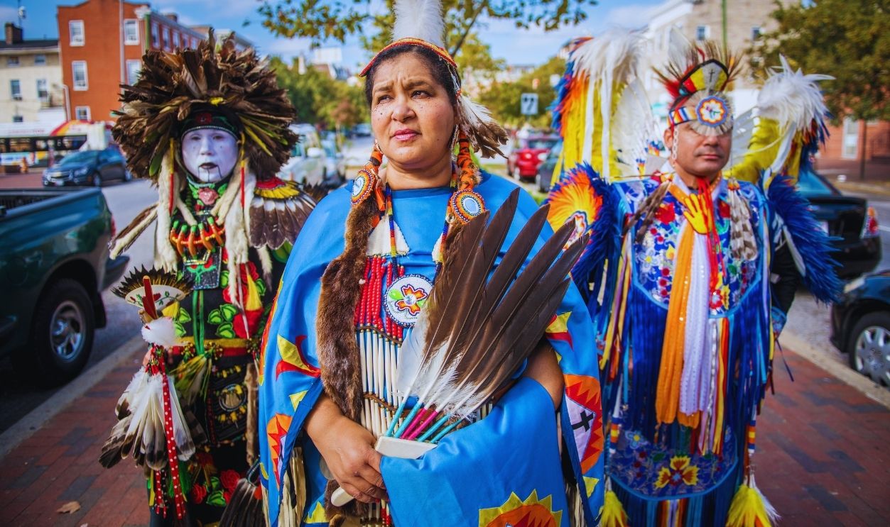 Gettyimages - 1162779694, Group of Native Americans dancers belonging to the Lumbee tribe stand in traditional costumes on the streets of Baltimore, Maryland