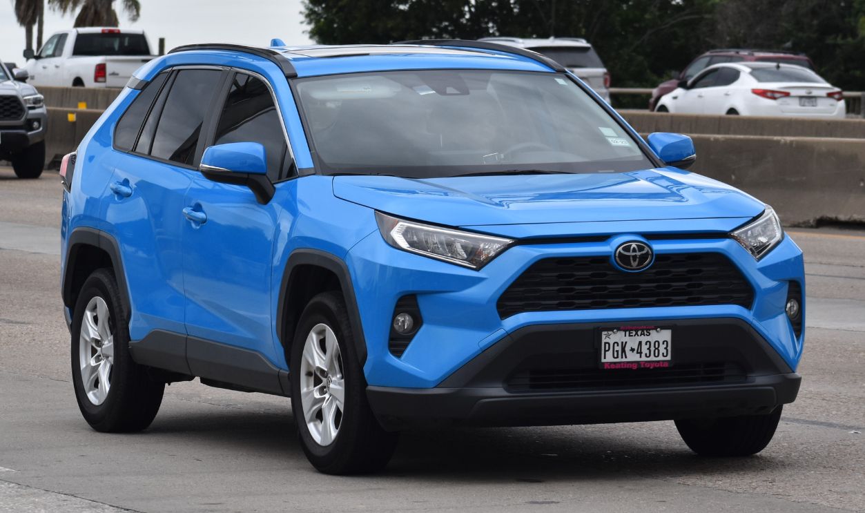 A portrait of a blue Toyota Rav 4 traveling down a highway in moderate traffic