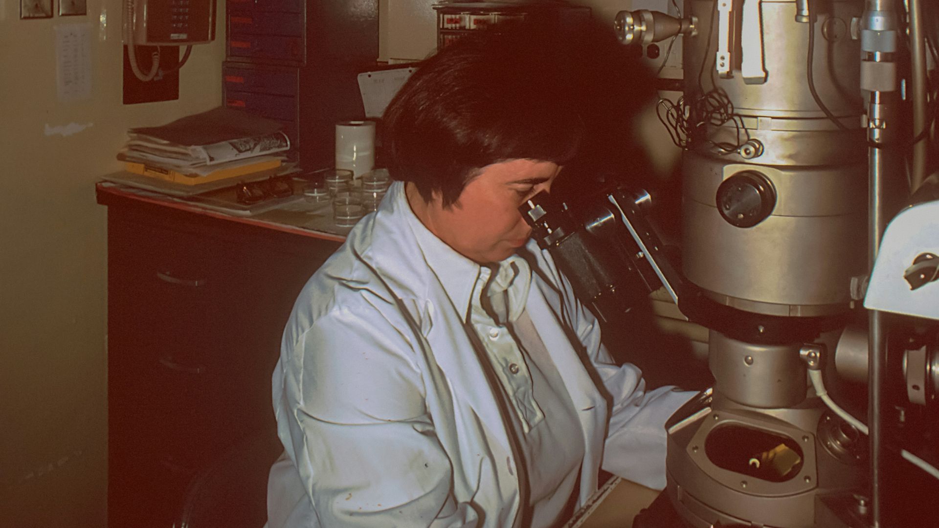 a woman looking through a microscope in a lab