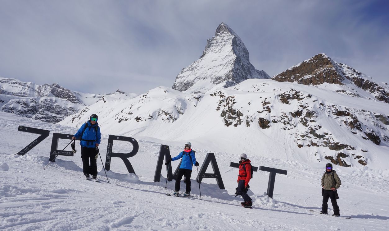 Zermatt, Switzerland - 14 March 2024: Four female skiers / snowboarders are stand at the ZERMATT sign in front of the Matterhorn, close to the Schwarzsee cable car station.