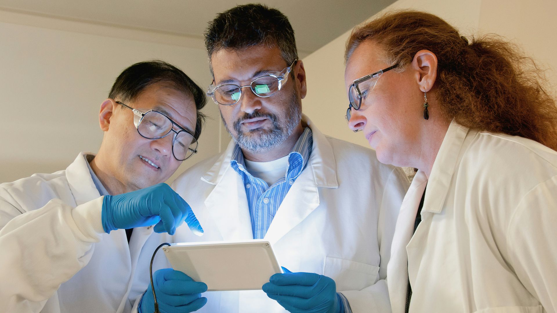 three people in lab coats looking at a tablet