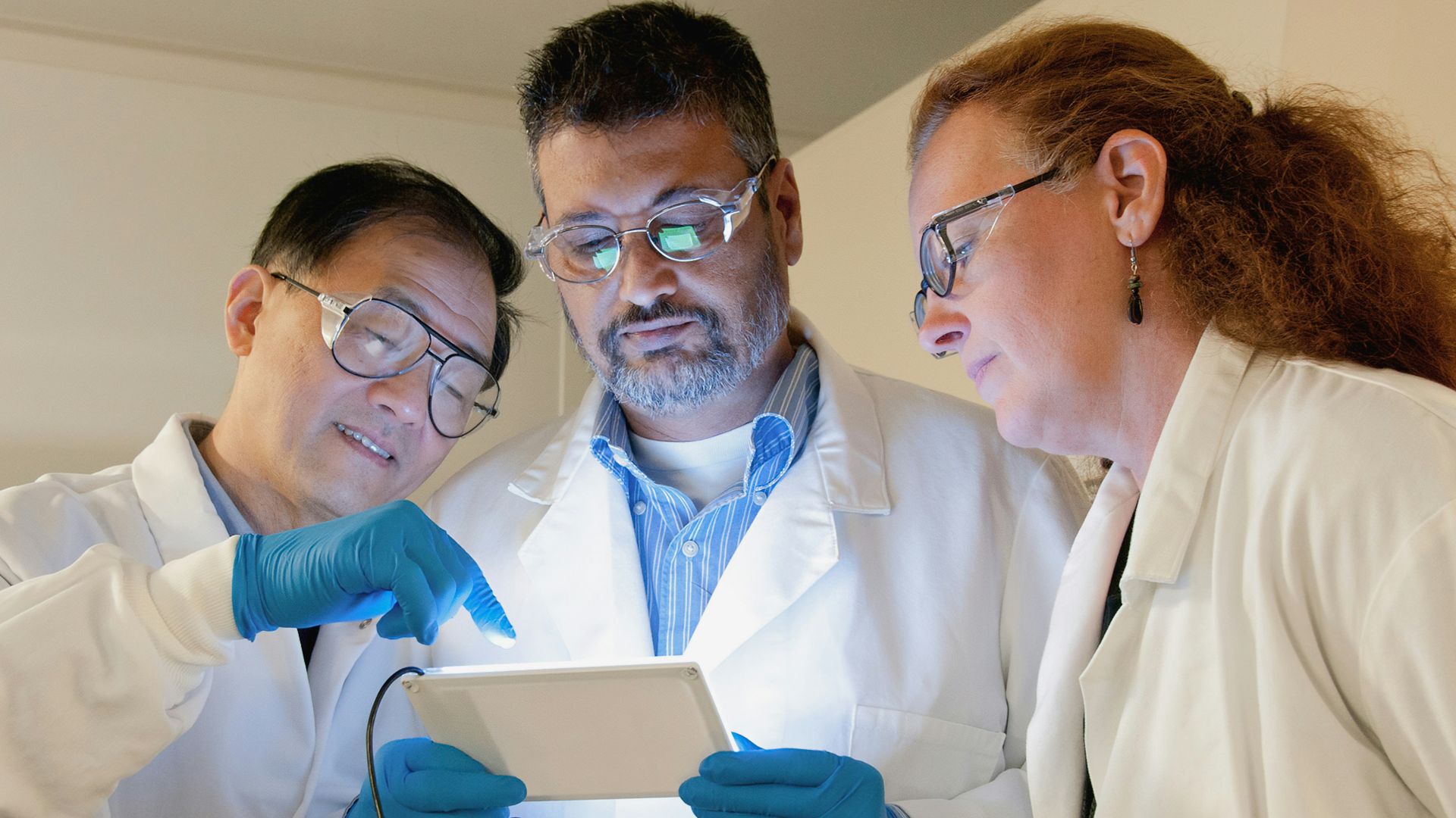 three people in lab coats looking at a tablet