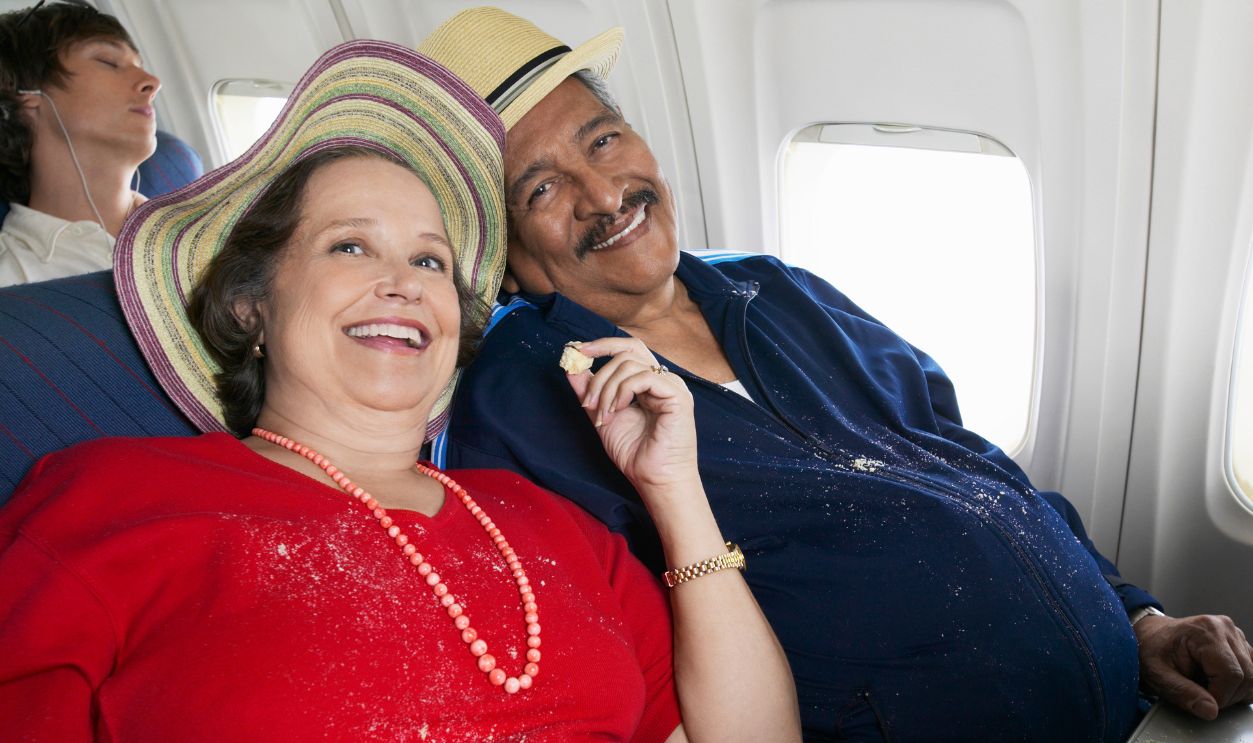 Overweight Senior Couple Sit on a Plane Sharing Cake, Crumbs on Their Clothes