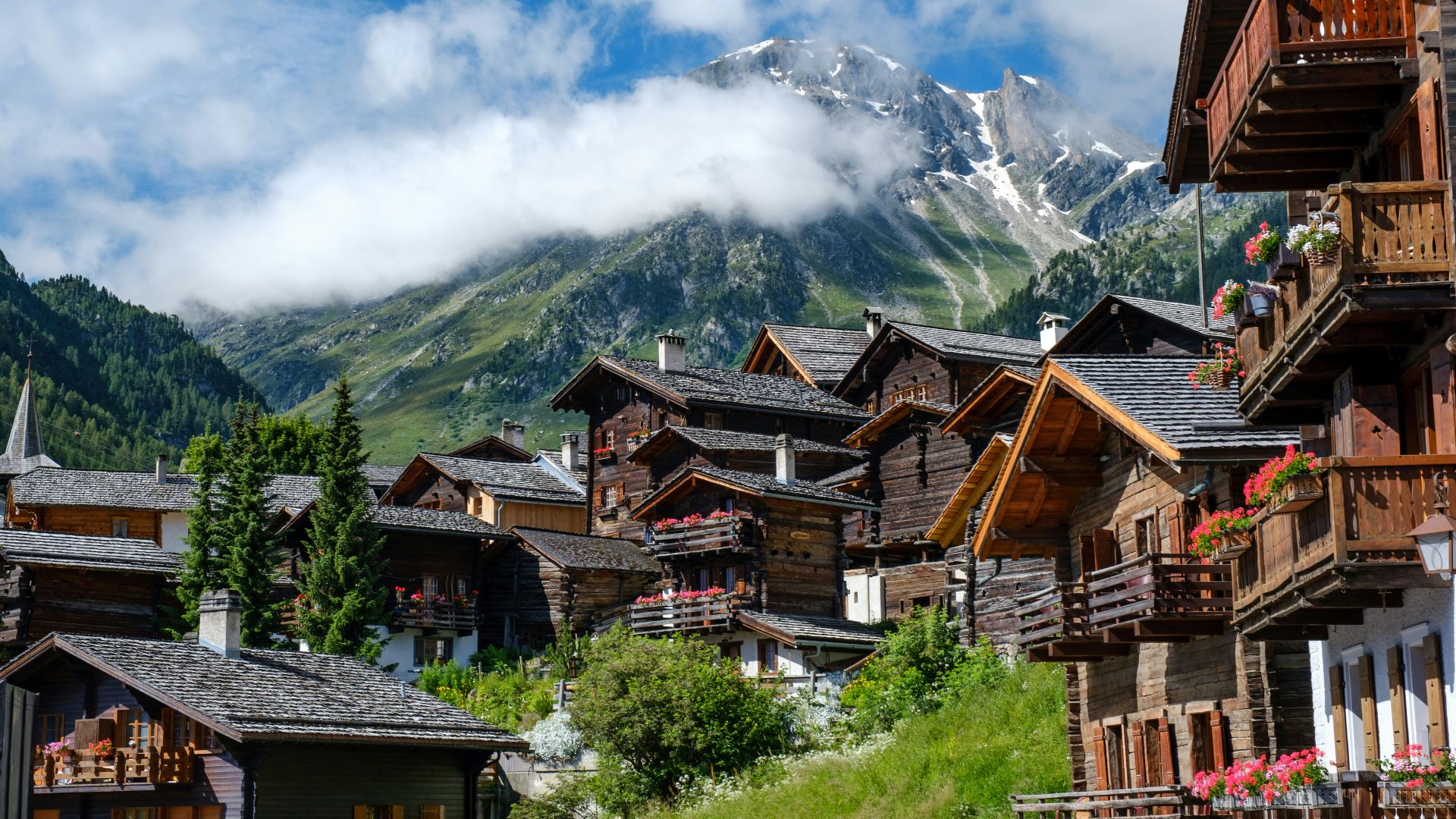 brown wooden houses near green trees and mountain under white clouds during daytime