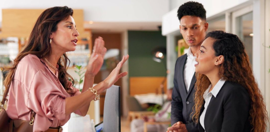 Shutterstock - 2542553393, Frustrated, receptionist and people at front desk of hotel for angry client, lost luggage and check in problem. Customer service, concierge and late booking with woman in lobby for appointment error.