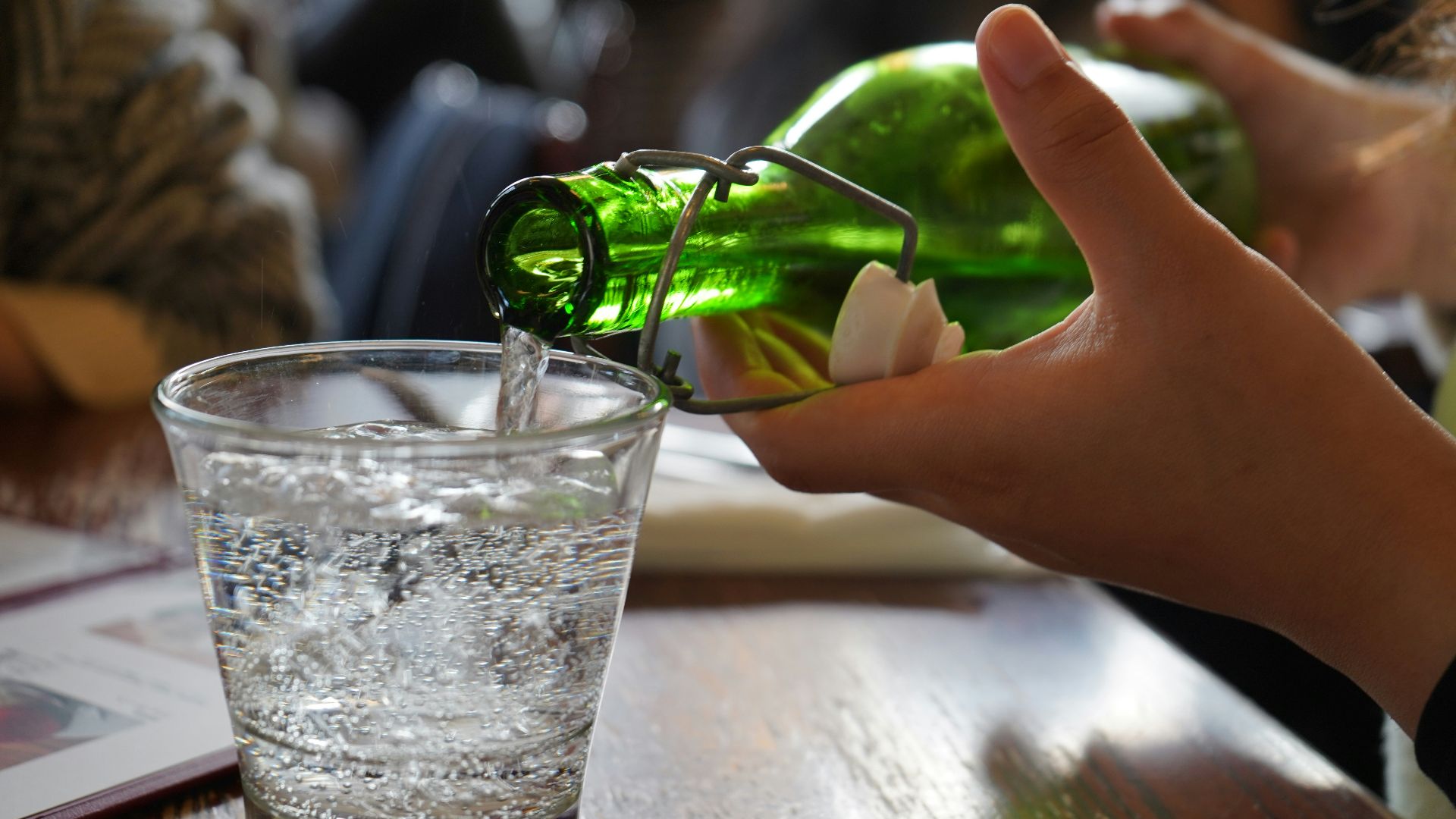 a hand holding a green object above a glass of water