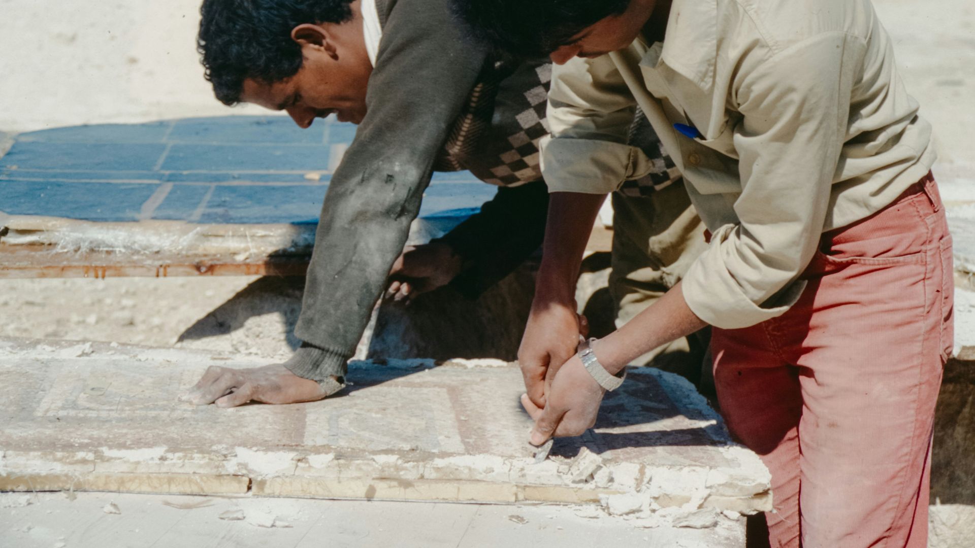 Two young men working on stone blocks outdoors.