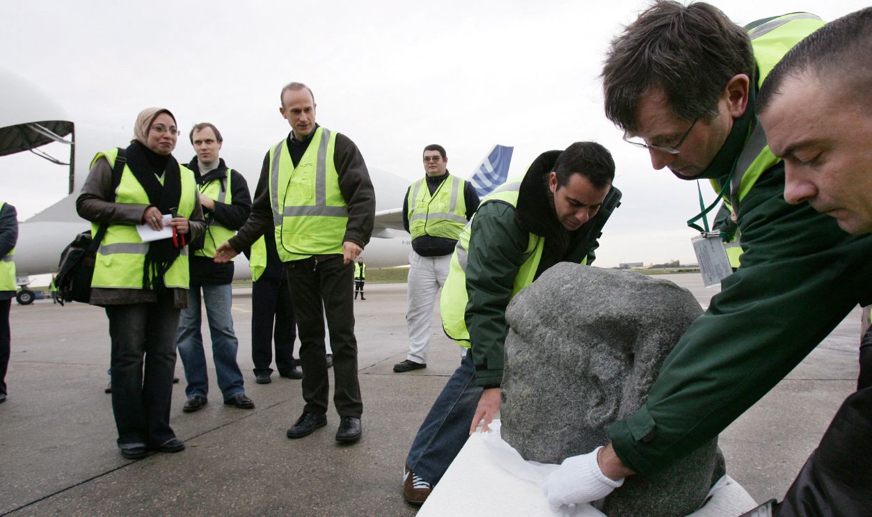 Gettyimages - 155702010, FRANCE-EGYPT-ARCHAEOLOGY-EXHIBITION The statue of Cesarion, is unwrapped on the tarmac, as French archaeologist Franck Goddio (3rdL) and Egyptian curator Snaa Fouad Zaki (L) from Cairo's Museum, look on, upon its arrival aboard a Beluga plane from Cairo, at Roissy airport, near Paris, 16 November 2006. The black granite statue, shown in Paris museum, le Grand Palais in the exhibition 