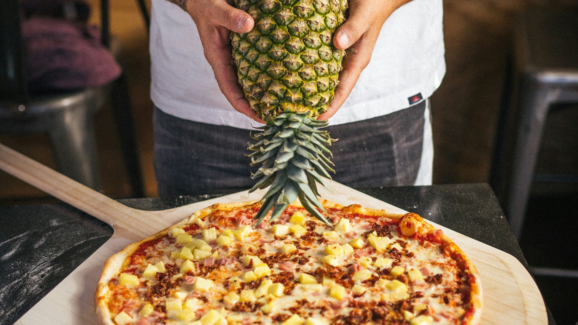 a man holding a pineapple on top of a pizza