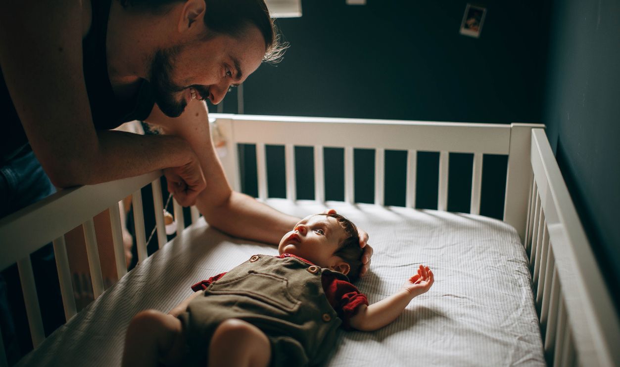 A father lovingly interacts with his baby in a warm, cozy bedroom setting