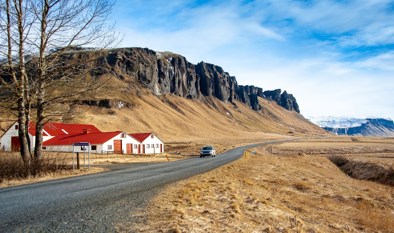 Ring Road No.1, near Skeidararsandur, southern Iceland. Picturesque scene, red roofed farm houses, snow capped mountain range, long road ahead.