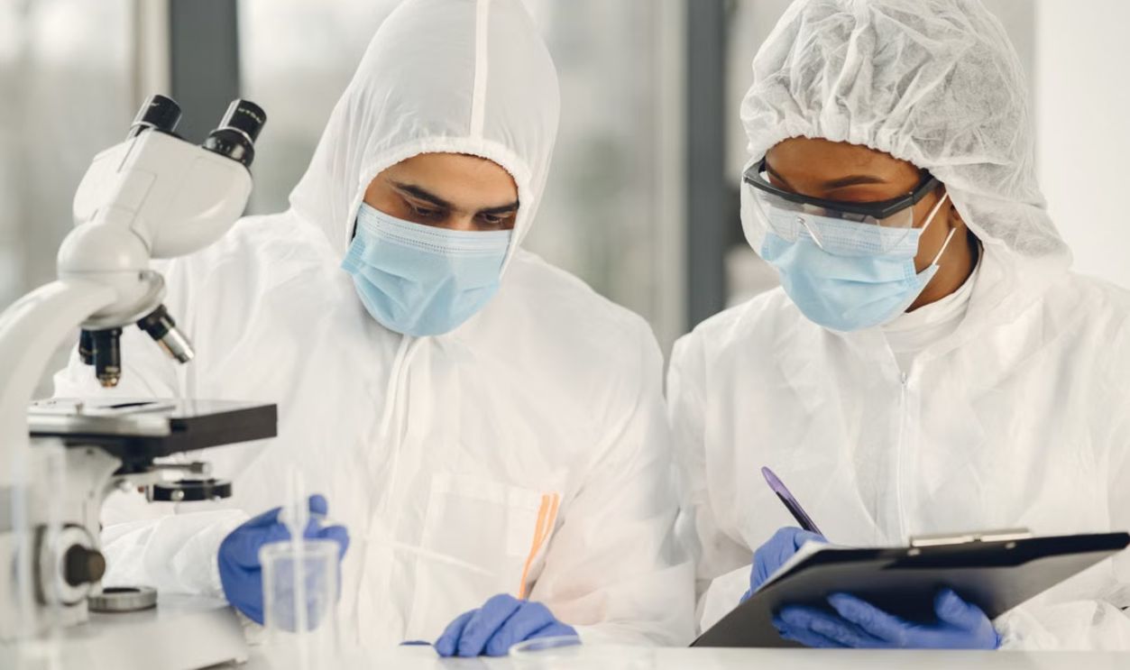 Two scientists in hazmat suits working with a microscope and notes in a laboratory setting