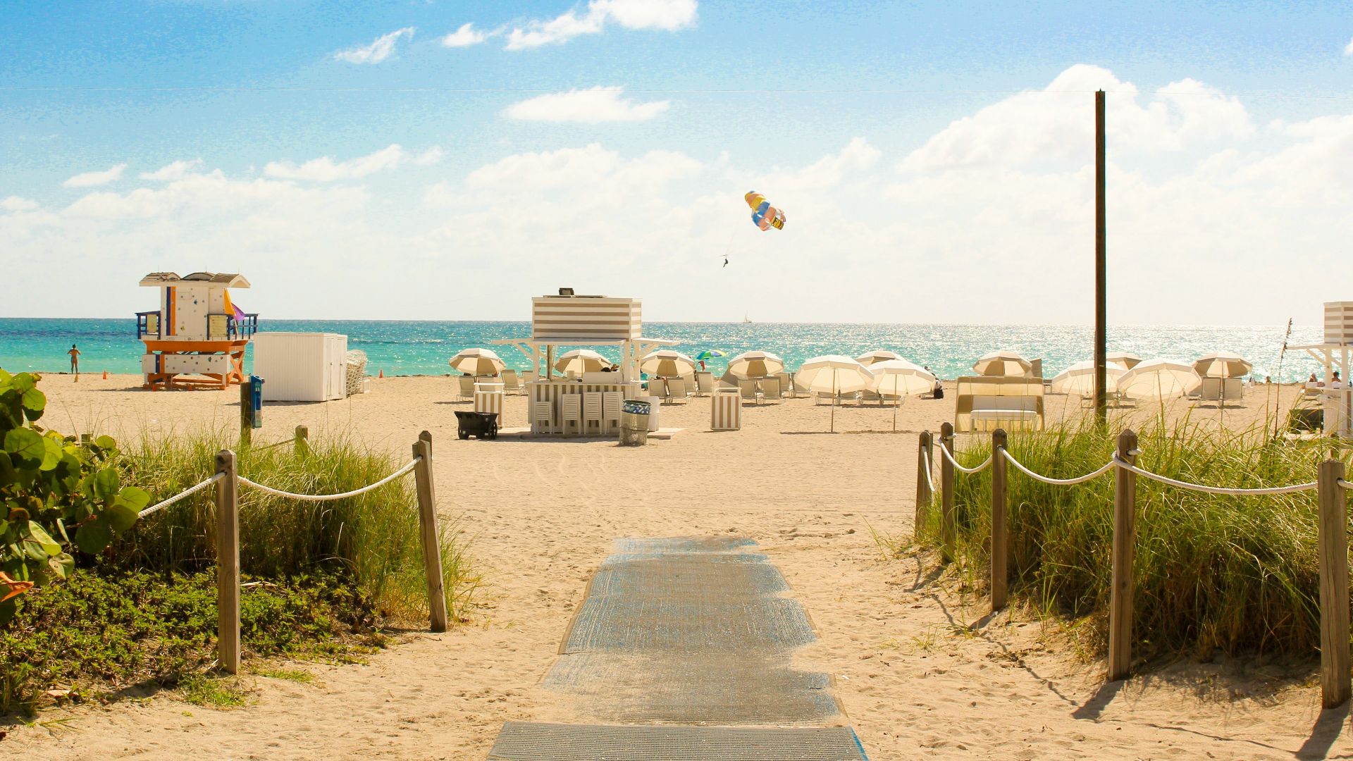 gray pathway leading to parasol, lifeguard house, and sea a daytime