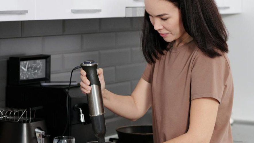 Woman Preparing Food for Children in a Kitchen using a immersion blender.