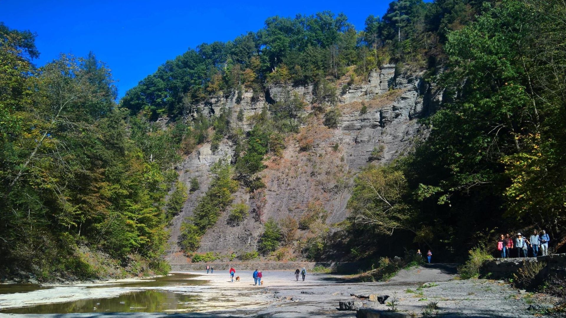 The walls of the Taughannock Creek gorge make an imposing backdrop for park visitors walking along the Gorge Trail and/or wading in the nearly dry creekbed during a period of unusually low water flow, Taughannock Falls State Park, New York, October 2017.
