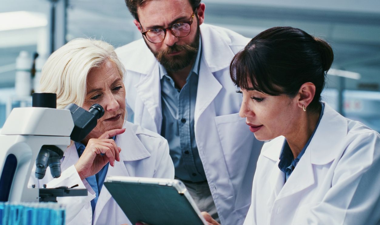 Microscope, science and tablet with team in laboratory together for development or research. App, feedback and talking with scientist people at work on clinical trial, medical industry or study