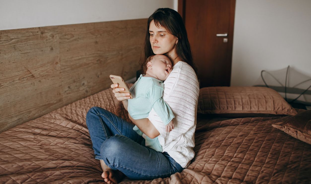 A mother holds her sleeping baby in a relaxed moment inside a bedroom