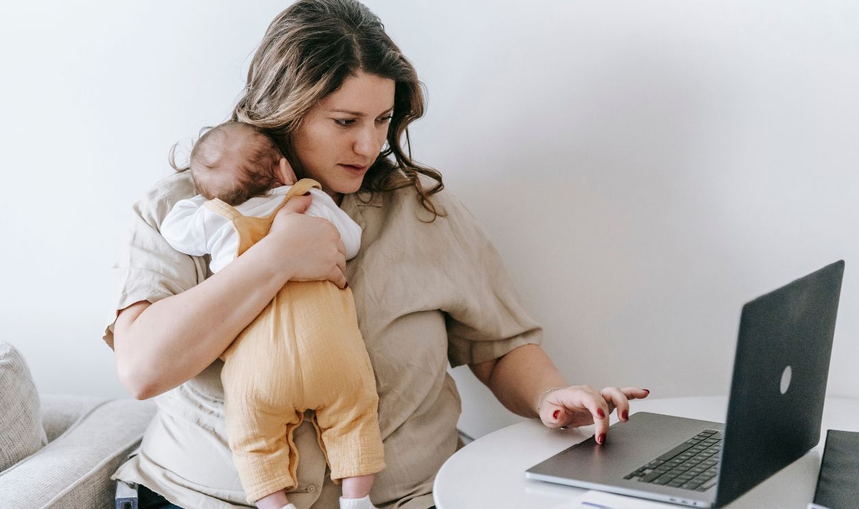 Mother multitasking with baby in arms and laptop