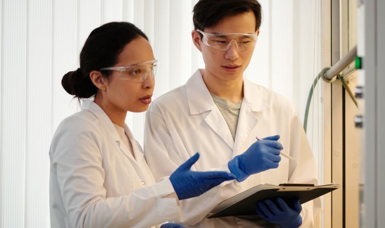 Researchers discussing data in a laboratory setting, wearing safety gear and blue gloves