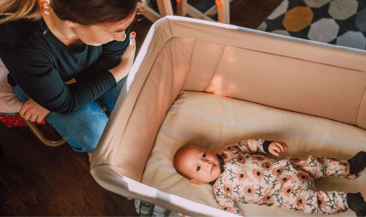 A mother lovingly watches over her baby in a crib