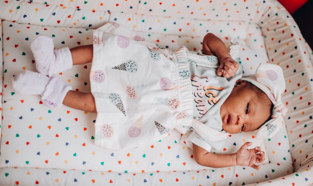 Cute baby lying on a colorful heart-patterned blanket