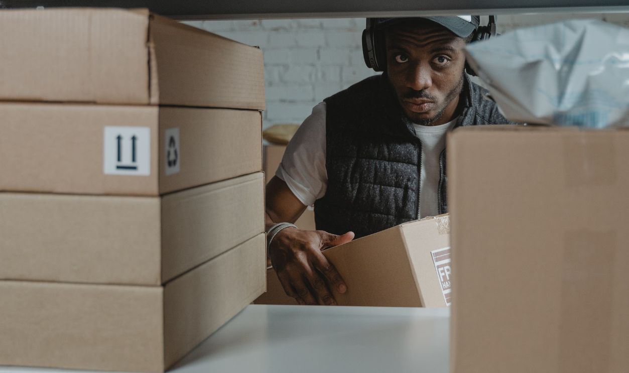Man organizing packages on shelves in a warehouse setting with cardboard boxes.