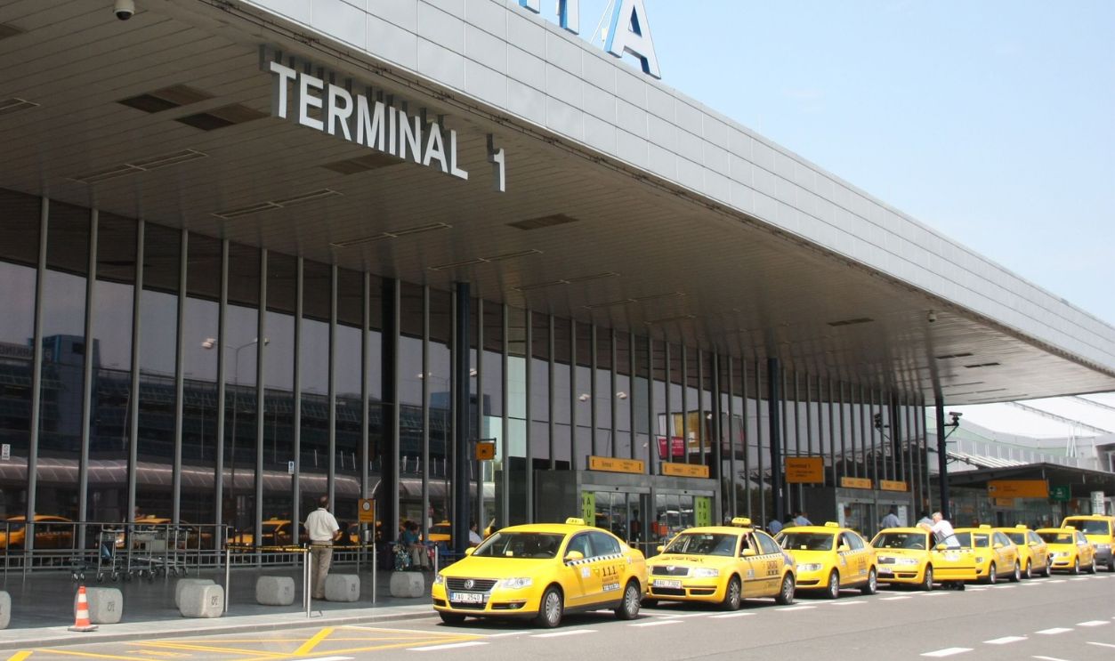 Exterior view of Praha Airport's Terminal 1 with a line of yellow taxis 